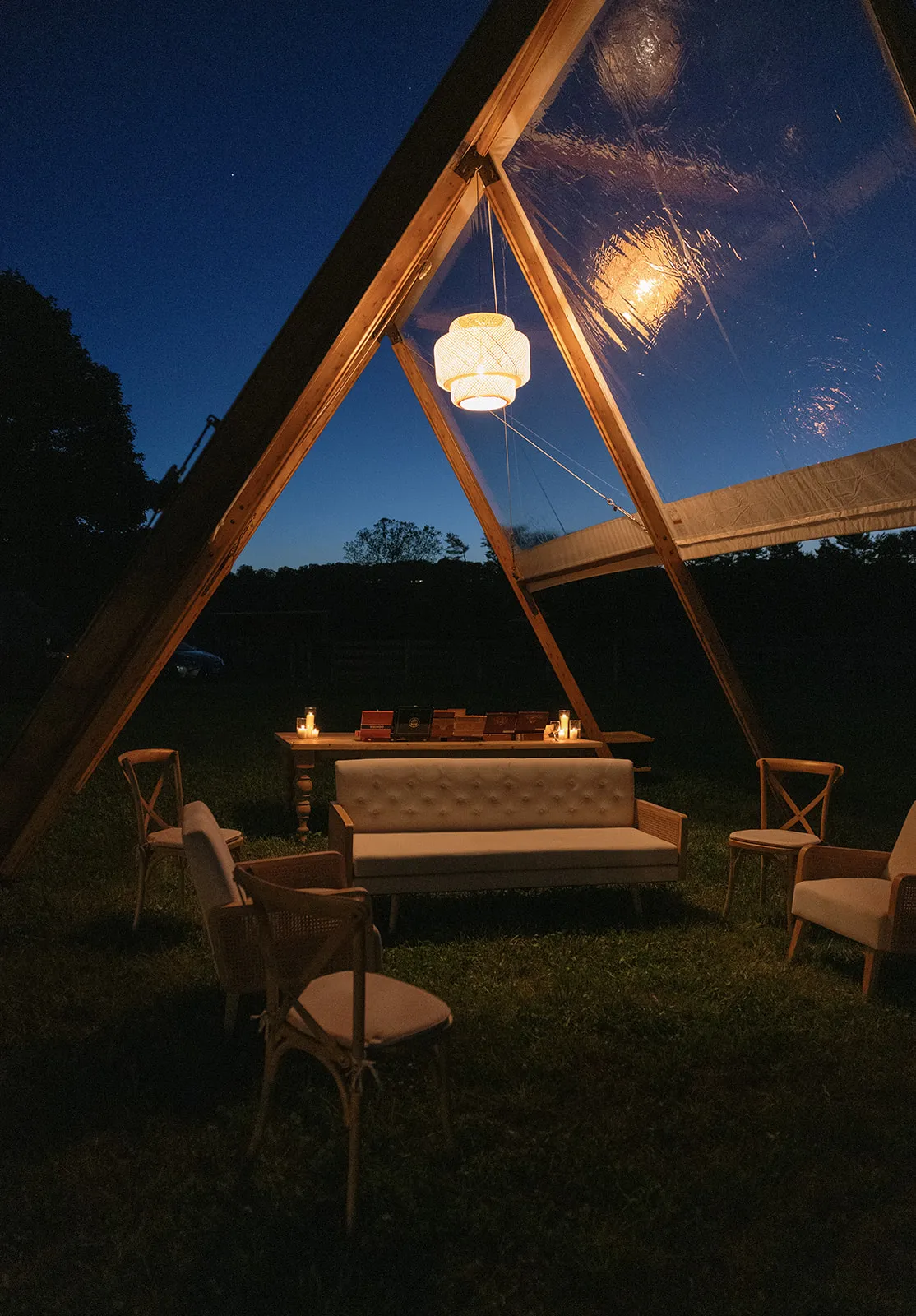 Lounge seating and woven pendant lantern inside an Adena A-frame tent at dusk