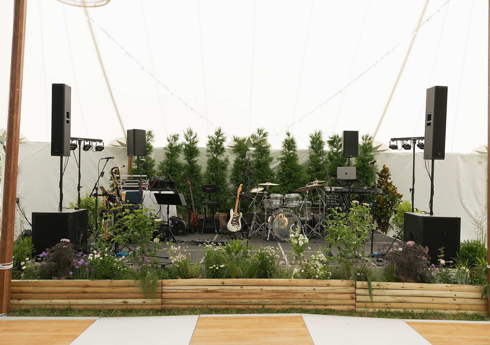 Band stage dressed in greenery inside a wedding tent