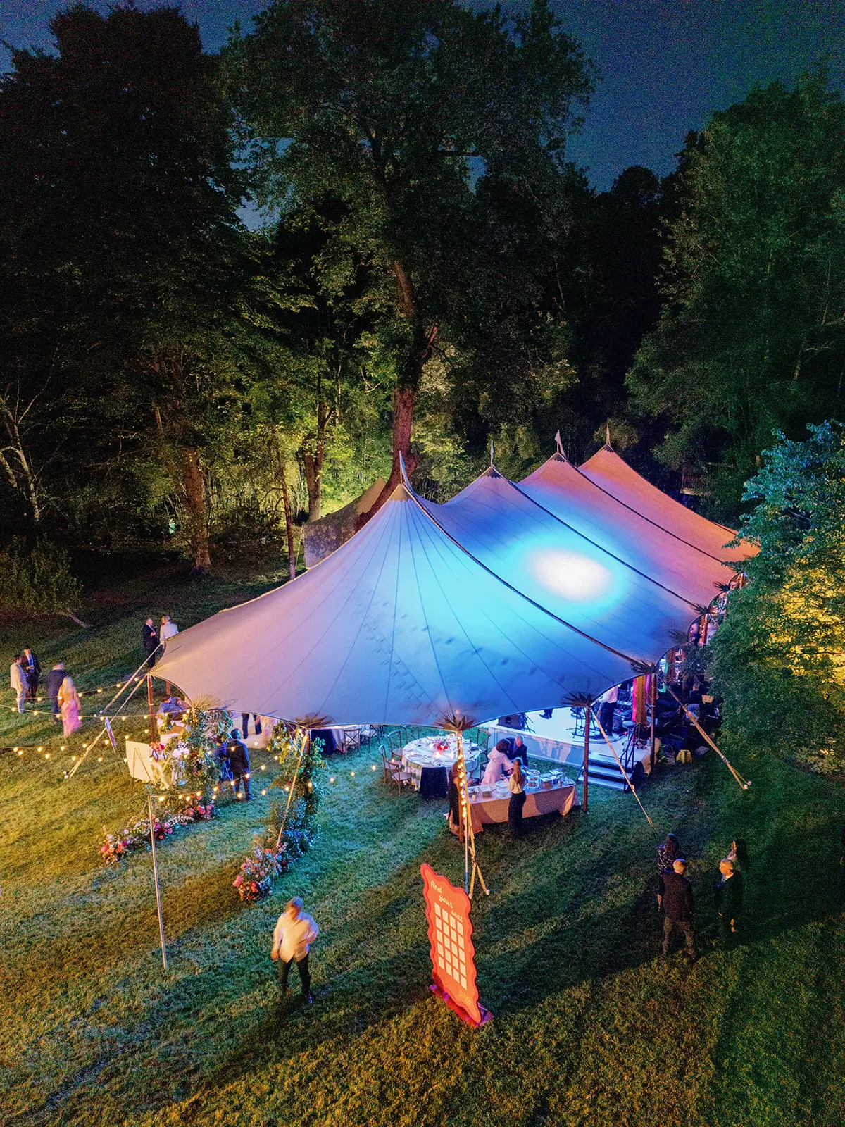 Aerial view of a glowing sailcloth wedding tent at night with string lights