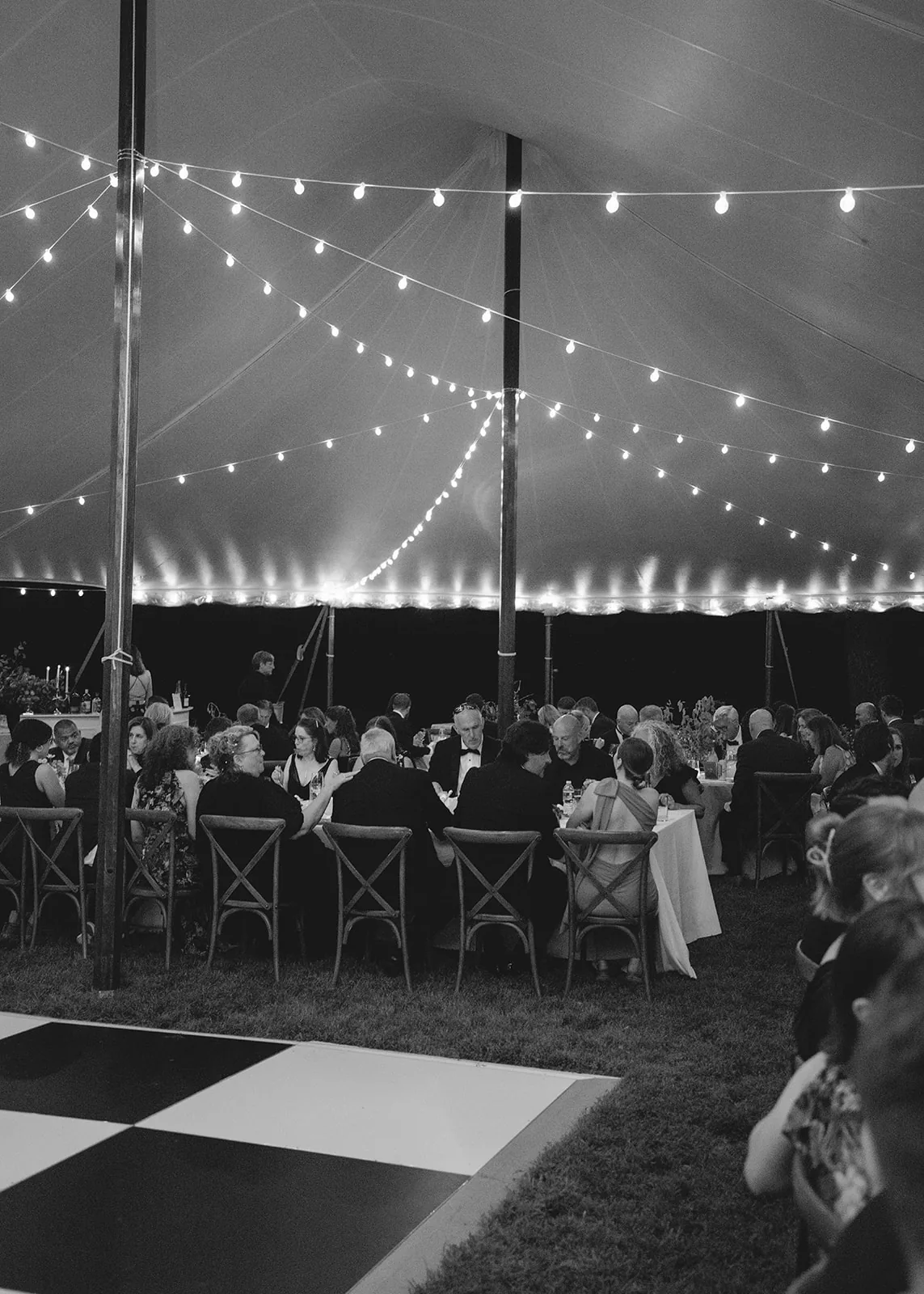 Guests dining under a lit sailcloth wedding tent at night