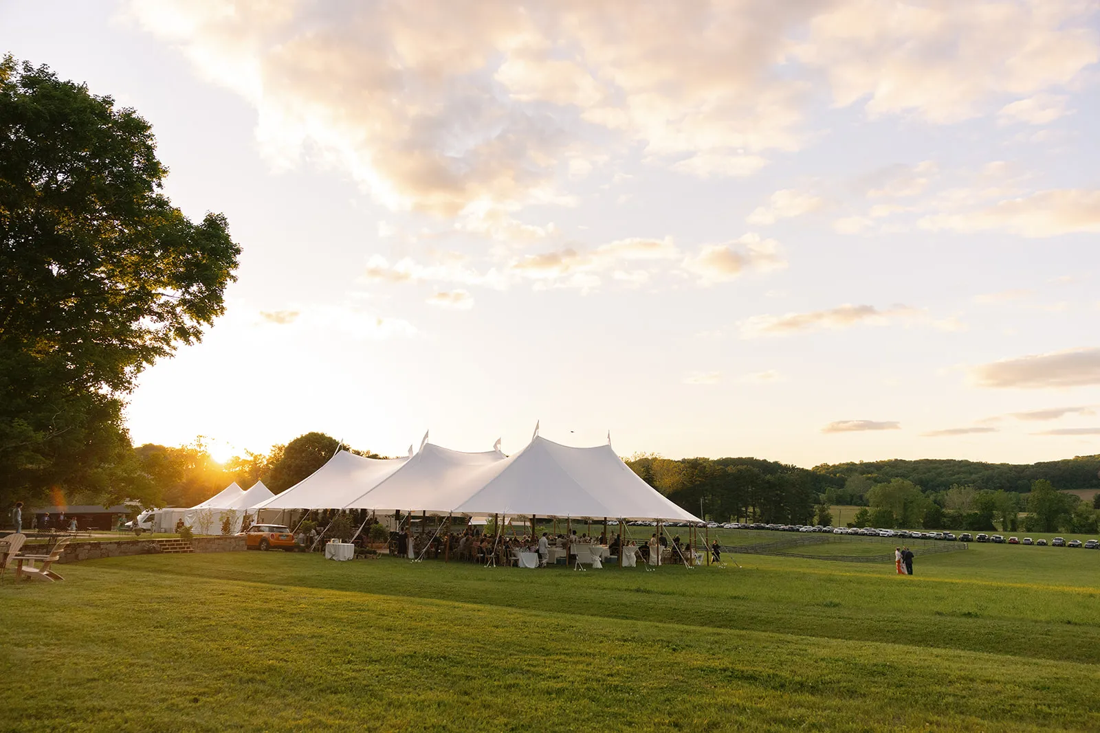Sailcloth wedding tents in an open field at sunset with guests dining inside