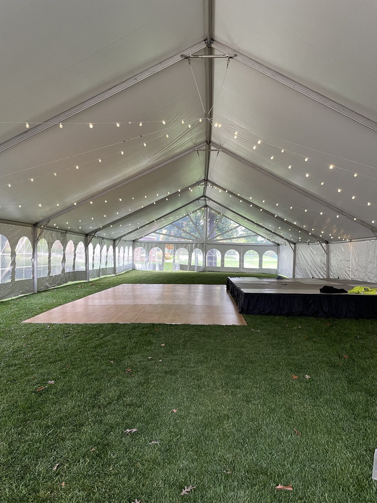 String lights over a dance floor and stage inside a tent