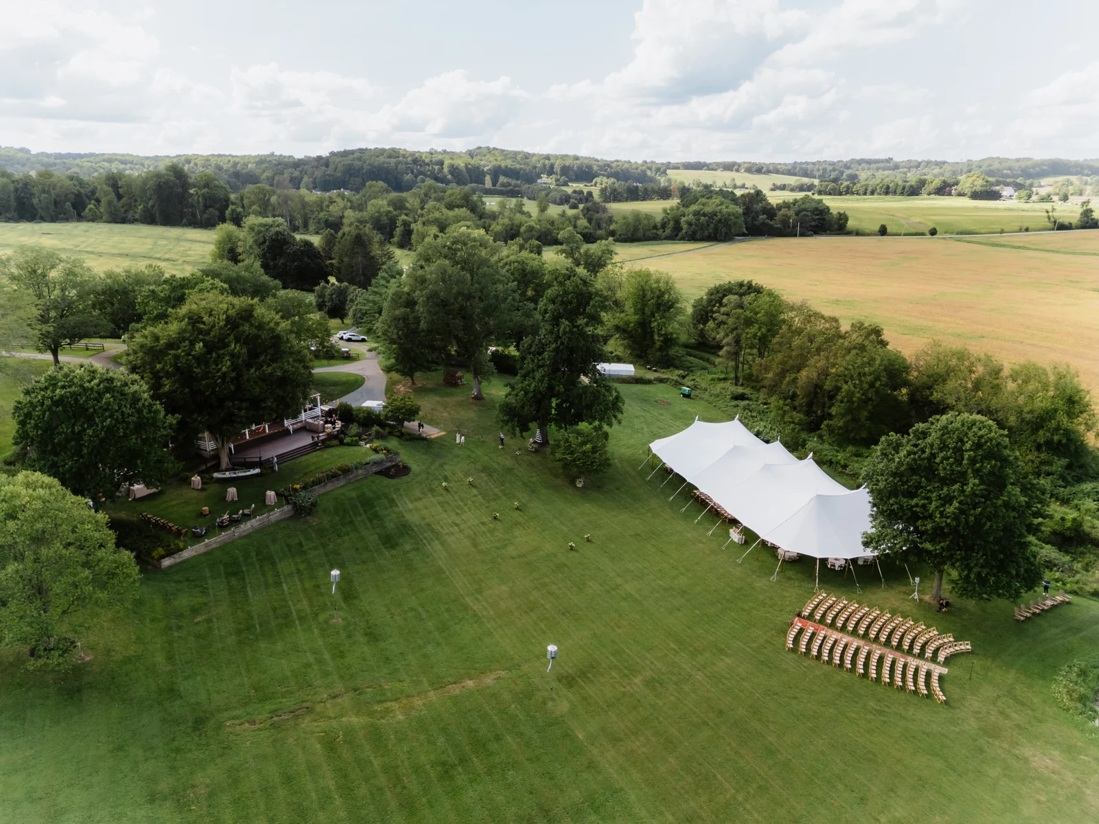 Aerial view of a sailcloth wedding tent and ceremony seating on a lawn beside a pond