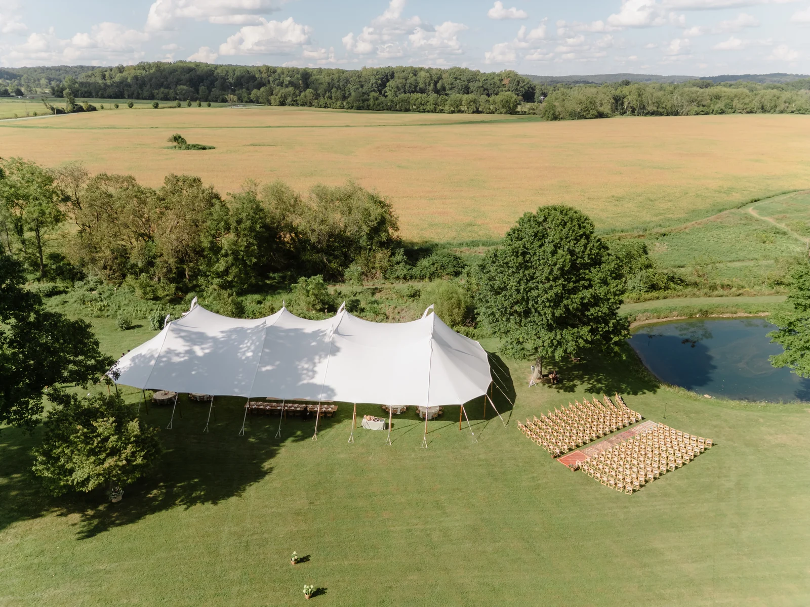 Wide aerial view of a sailcloth wedding tent and pondside ceremony seating