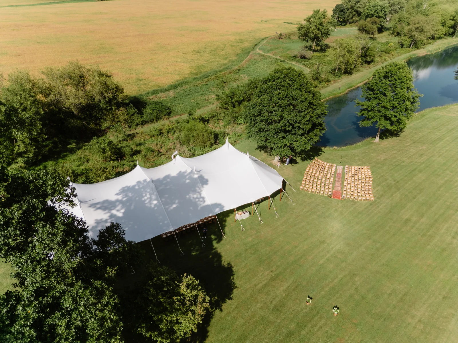 Aerial view of a sailcloth tent framed by trees beside a pond