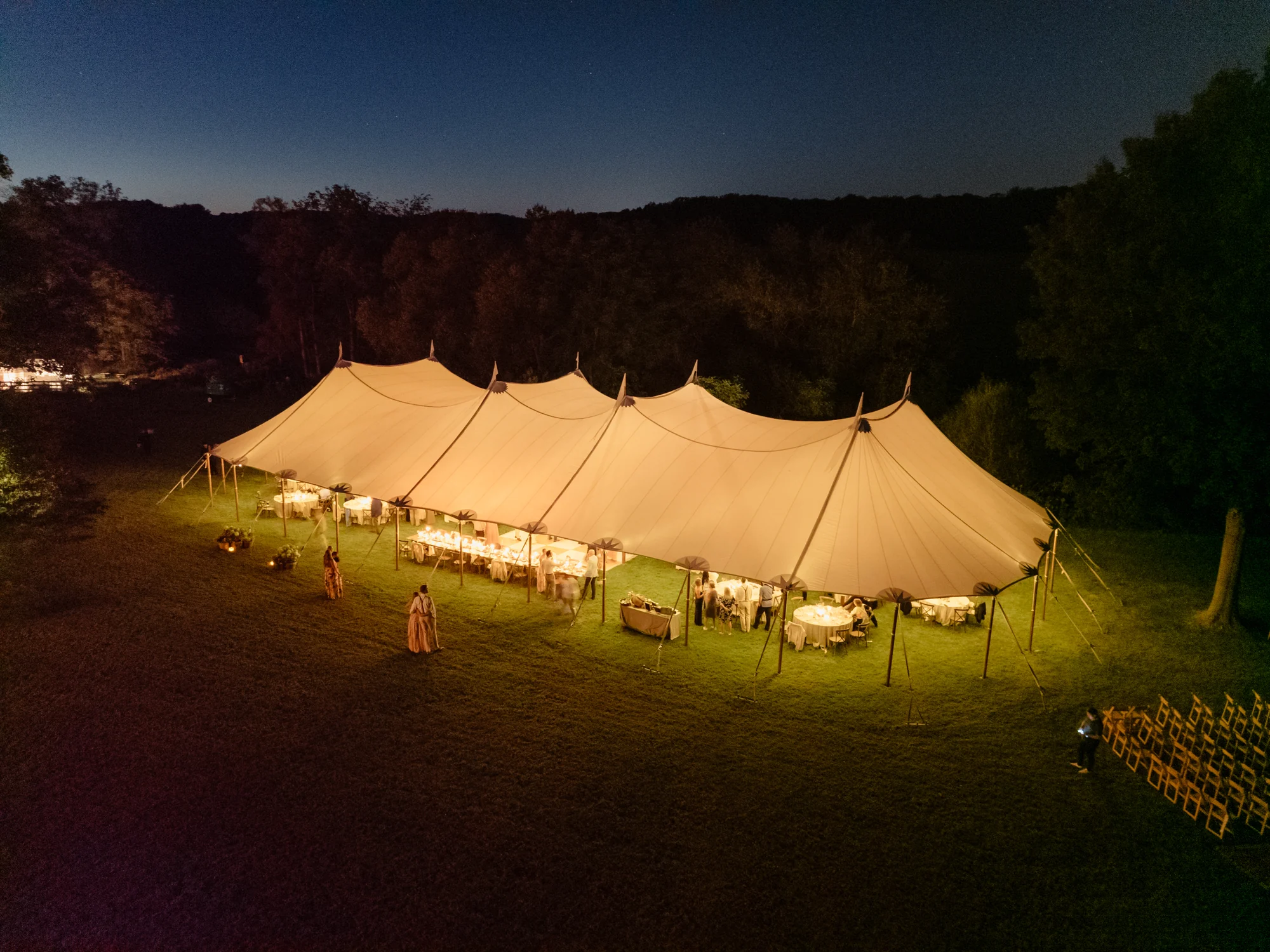 Sailcloth wedding tent glowing at night, with guests and reception tables beneath the canopy