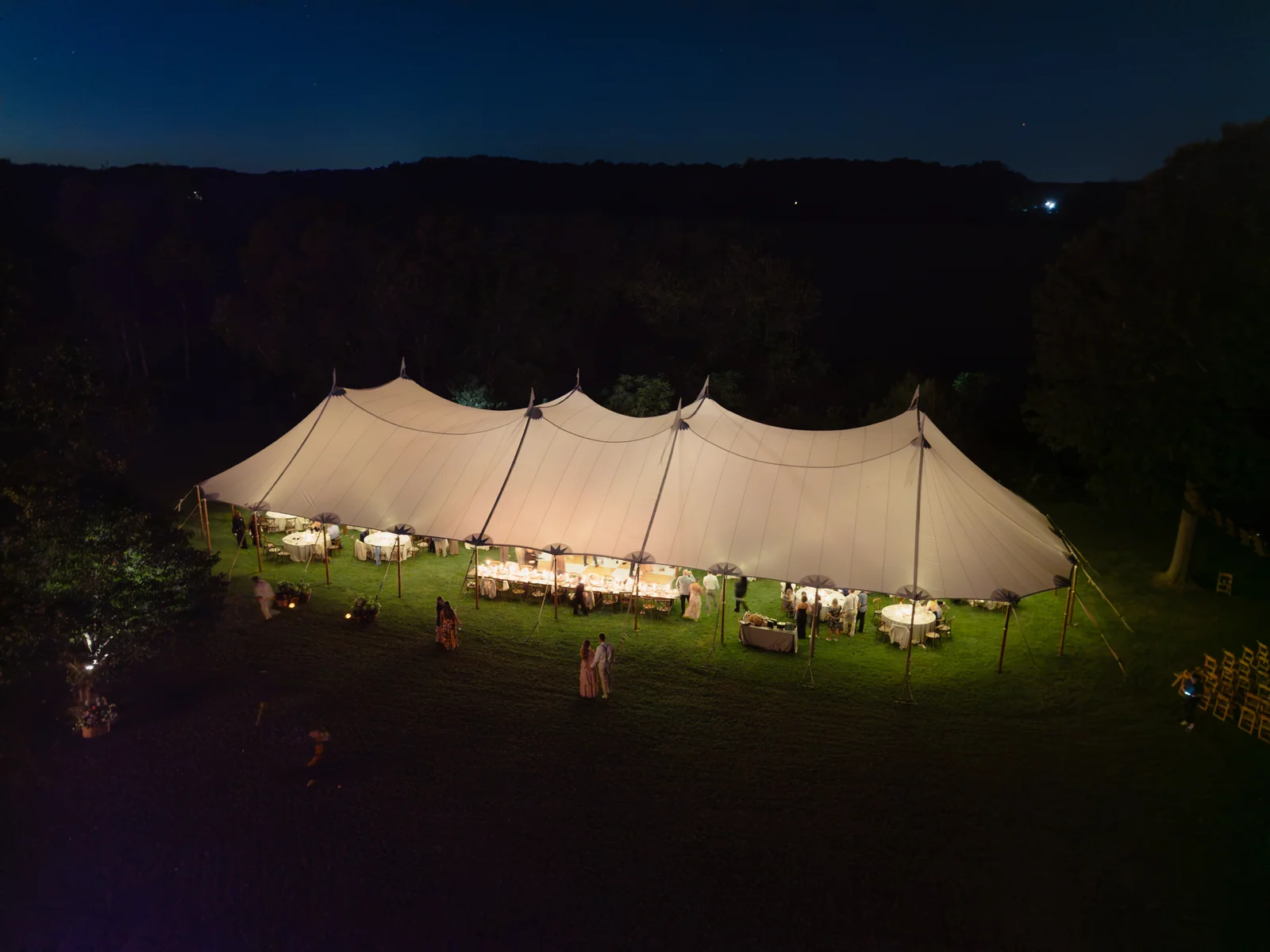 Illuminated sailcloth wedding reception tent beneath a dark evening sky