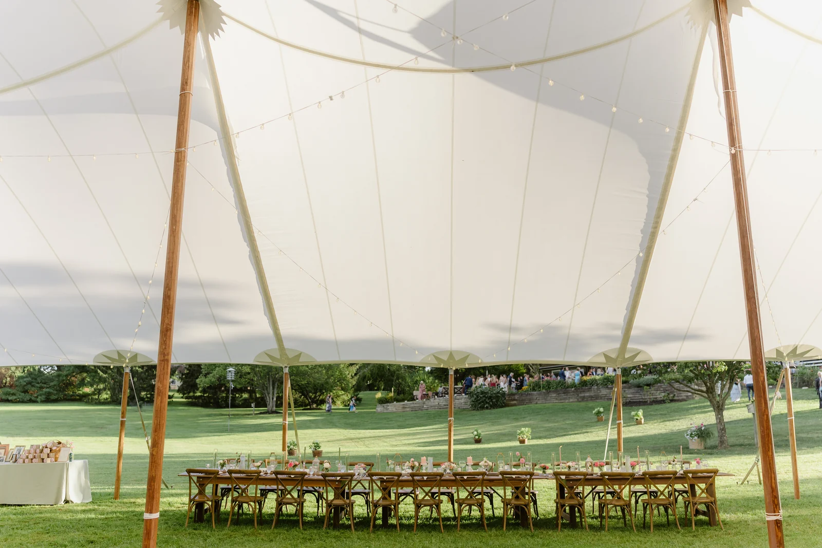 Reception tables beneath a sailcloth canopy with wooden poles and string lights