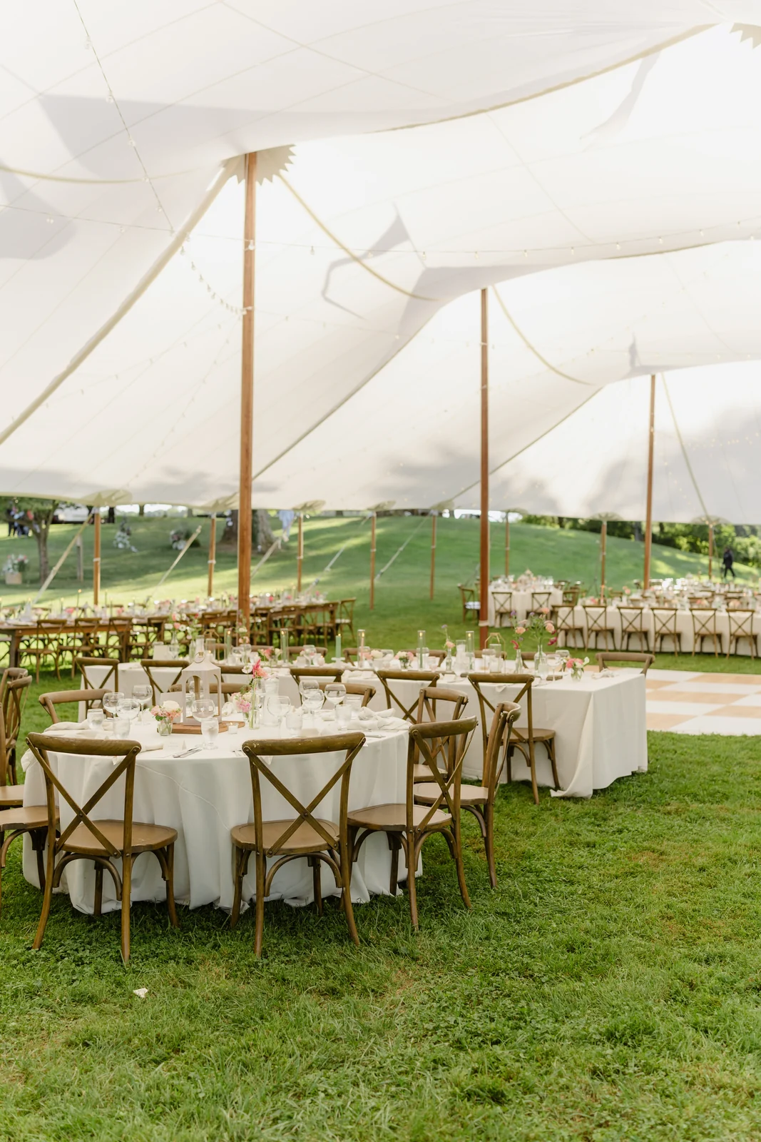 Round reception tables and cross-back chairs beneath a sailcloth wedding tent