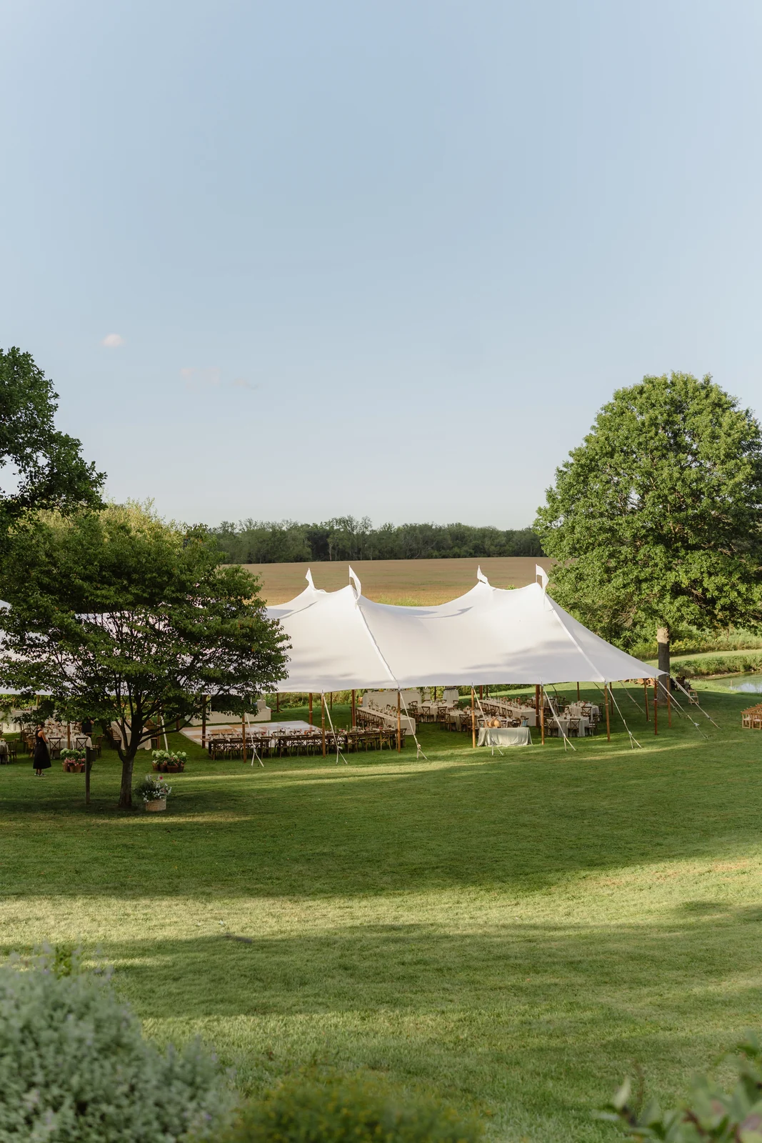 Sailcloth wedding tent viewed across a lawn framed by trees