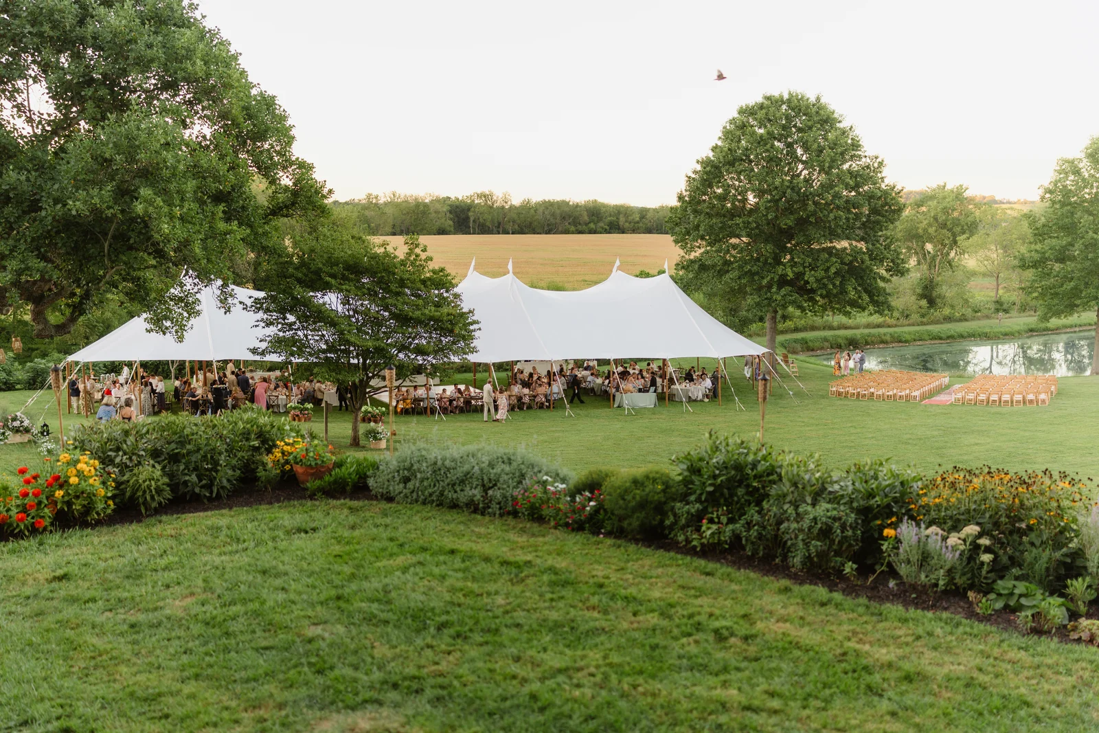 Guests gathered beneath a sailcloth wedding tent beyond a garden lawn
