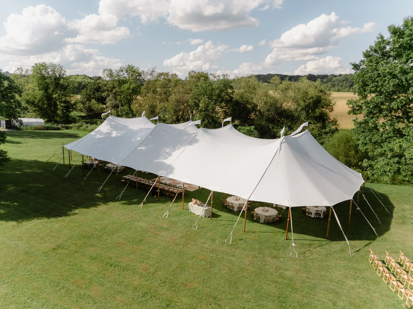 White sailcloth wedding tent with sweeping peaks and open sides on a green lawn