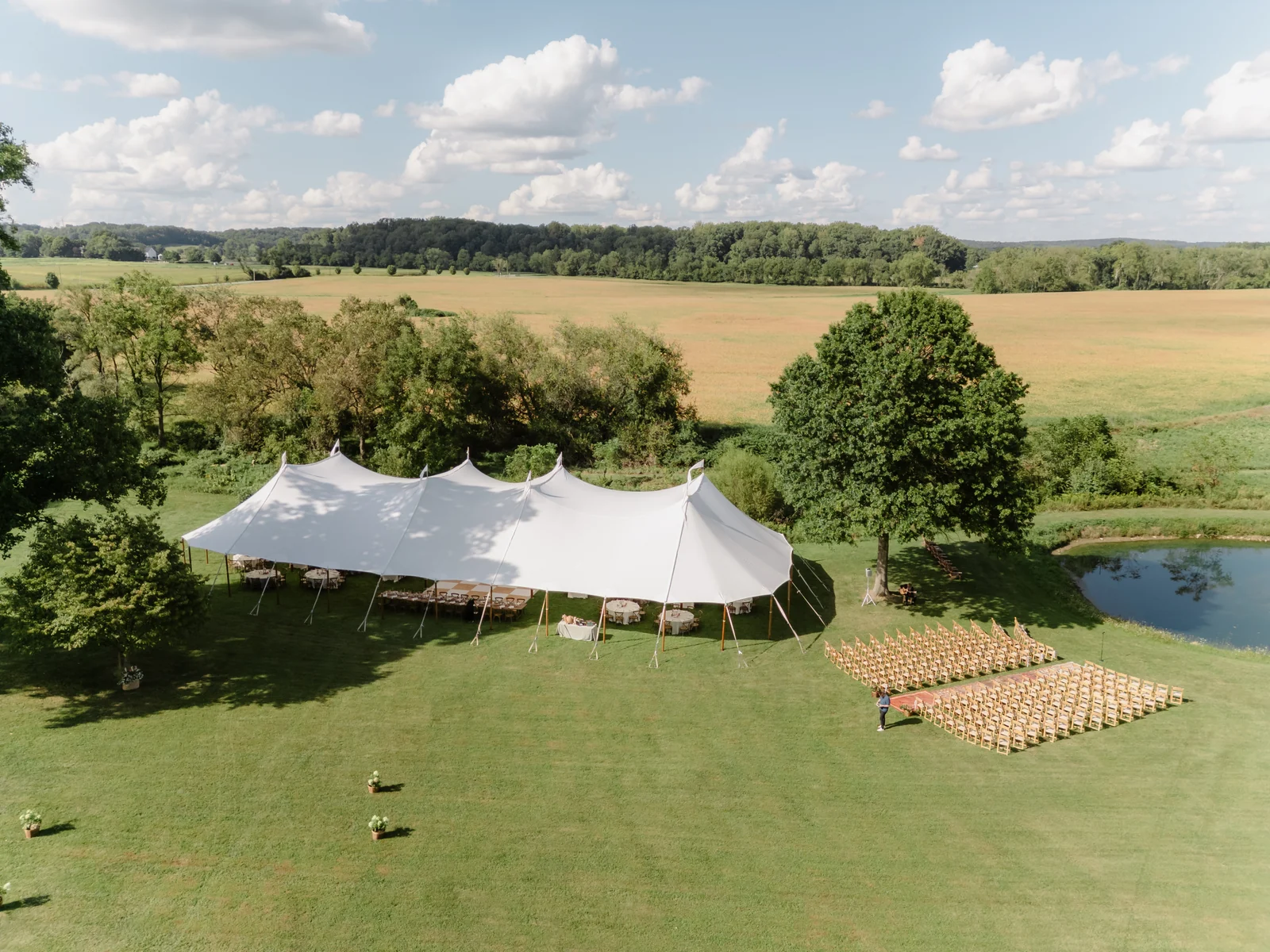 Sailcloth tent and wedding ceremony chairs beside a pond and open fields